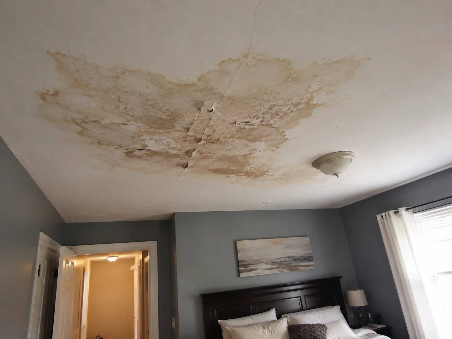 Bedroom ceiling with water stains, cracking, and peeling drywall before repair